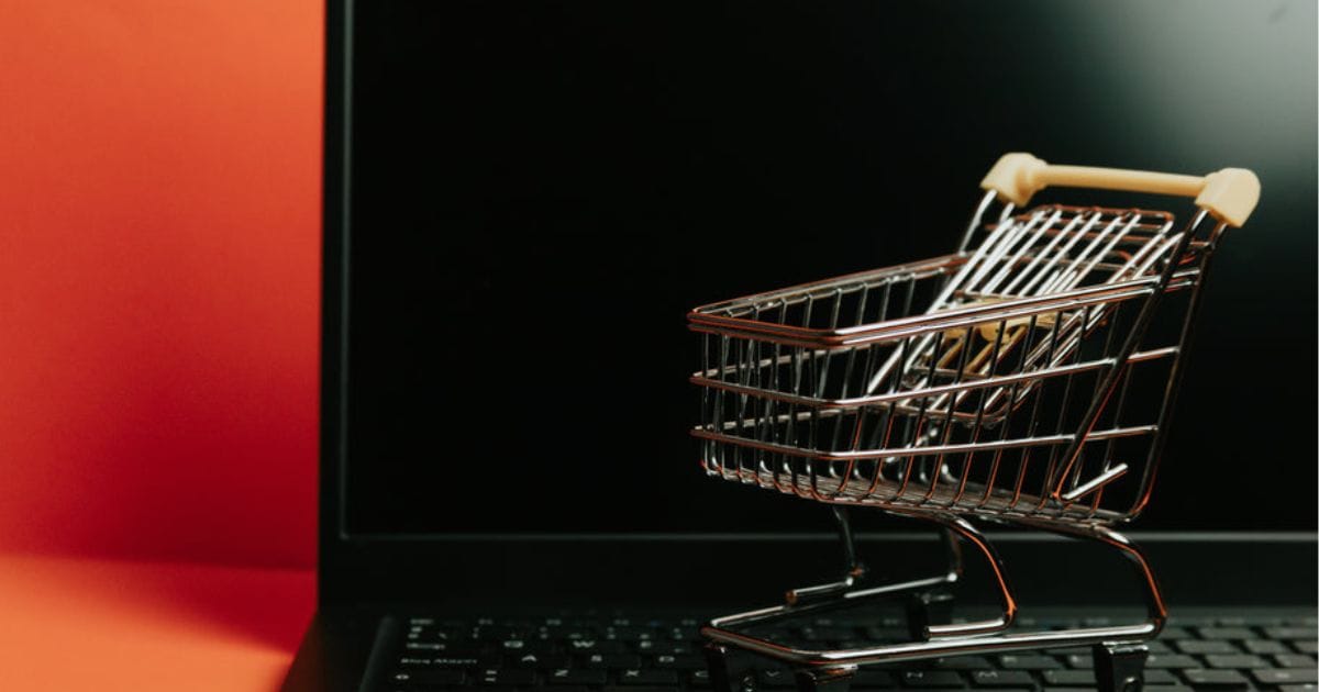 ノートパソコンの上に置かれたミニチュア版ショッピングカート